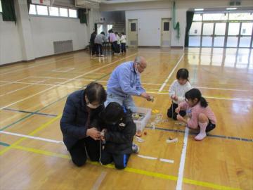 体育館でこまの紐の巻き方を教えてもらっている様子
