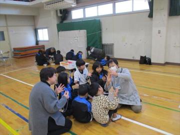 体育館で児童が講師からあやとりを教えてもらっている様子