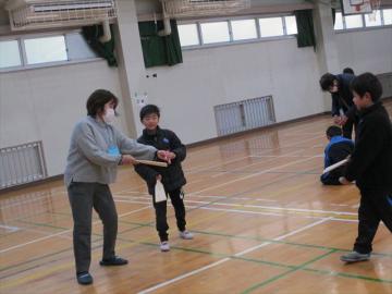 体育館で児童が講師から羽根つきを教えてもらっている様子