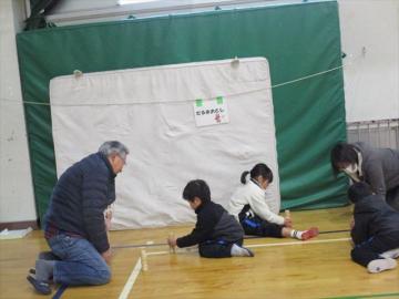 体育館で児童が講師からだるま落としのコツを教えてもらっている様子