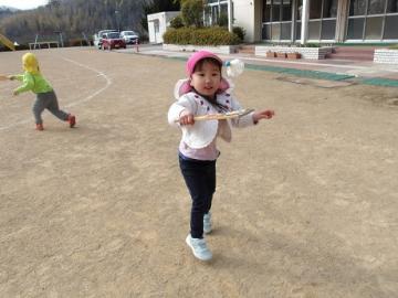 園児たちが校庭で羽子板を使い羽根つきをする様子