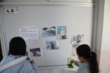 児童委員が校舎内の掲示板に写真を掲示している様子