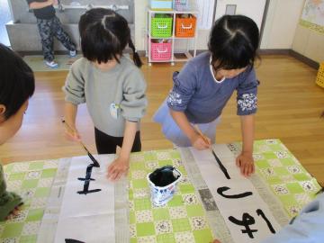 書初めでこまとはつもうでと書く子ども