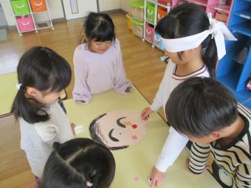 目隠しをして福笑いをする子供と、その様子を見ている子供たち