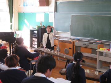 音楽教室の教壇に立ち、箏の爪の使い方を5年生に説明する講師