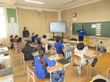 教室の教壇に立って説明している講師と、先生の説明を席に座って聞いている生徒たち