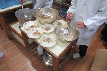 給食当番が鰯の竜田揚げと豆を取り分けている様子