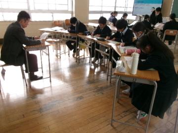 教室で講師の先生と対面に座る生徒達が、先生の話を聞きながらメモを取っている様子