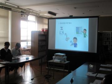 保健委員代表の生徒が椅子に座り、プロジェクターで資料内容を壁に写しながら取り組みの報告をする様子