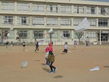 小学校の校庭で凧あげをしている園児たちの様子