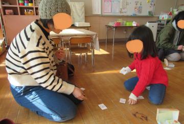 室内で読み札の裏を使ってお家の人と遊ぶ子どもの様子