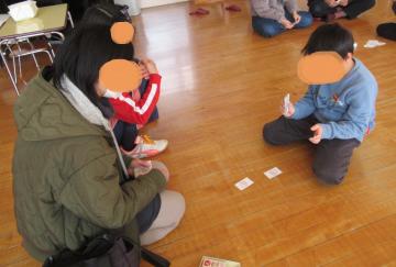 室内で読み札の裏を使ってお家の人とじゃんけんを楽しむ子どもの様子