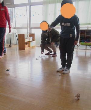 室内でお家の人とこまを回して遊ぶ子どもの様子
