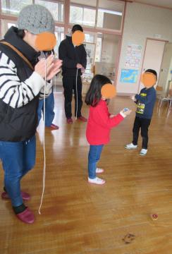 室内でこまに紐を巻いている子どもとお家の人の様子