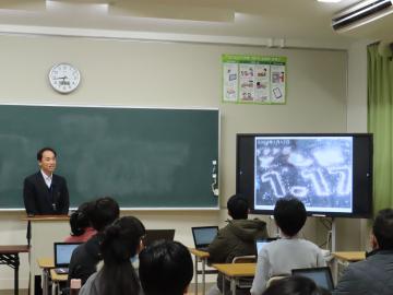 教室の教壇に立つ講師が「震災のつどい」の映像をテレビに流しながら説明するようす