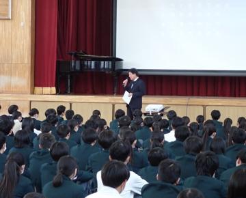 体育館の壇上前で校長の話を聞いている生徒たちの様子