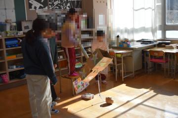 教室で椅子の上に立った児童が巨大けん玉で遊んでいるようす