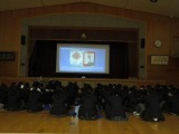 体育館でスライドを見ながらお話を聞く2年生の生徒たちの様子