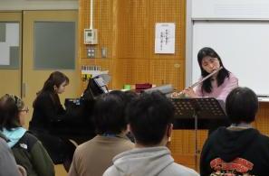 フルートの演奏をする女性と、その演奏を聴く生徒たちの様子