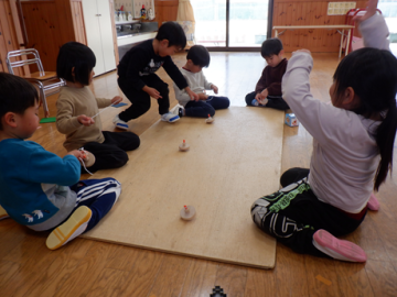 室内で座り、こまで友達と対決している園児たちの様子