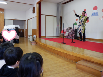 室内で演者の方とお猿さんによる猿回しの芸を見ている園児たちの様子