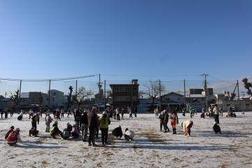 雪が積もった運動場で子どもたちが遊んでいる写真