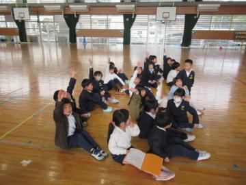 体育館でむかしあそびのふり返りの発表をする1年生の児童たちの様子