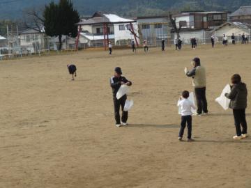 校庭で長寿会の皆さんにたこあげを教えてもらう1年生の児童たちの様子