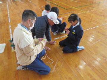 体育館で長寿会の皆さんにこまを教えてもらう1年生の児童たちの様子