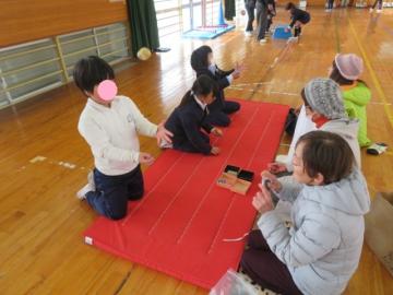 体育館で長寿会の皆さんにお手玉を教えてもらう1年生の児童たちの様子