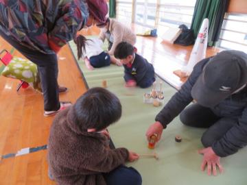 体育館で長寿会の皆さんにだるまおとしを教えてもらう1年生の児童たちの様子