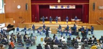 体育館の舞台で合奏する6年生と、その様子を見ている保護者たち