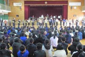 金管バンドのメンバーが体育館の全児童の前で演奏している様子