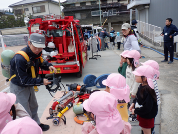 屋外で、消防車の中の道具について消防署の職員から説明を受ける園児たちの様子