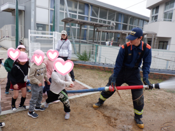 屋外で消防署の職員から放水の説明をしてもらっている園児たちの様子