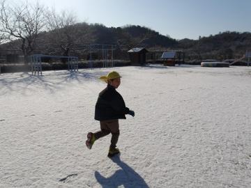 幼児が雪で真っ白になった園庭を走る様子