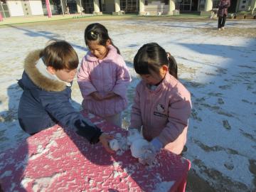 雪が降った園庭で雪だるまを作る園児たちの様子