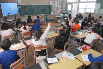 4年生が教室の自席に座って挙手をしている様子