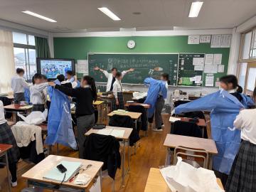 生徒たちが教室で臨床工学技士体験で医療用ガウンを試着する様子