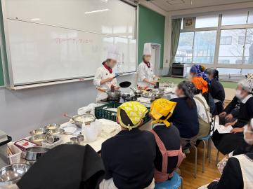 生徒たちがパティシエ体験で、椅子に座って説明を聞く様子