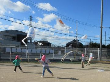 3人の園児たちが園庭で凧を揚げている様子