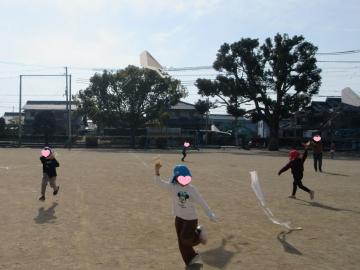 小学校の校庭で思い切り走って凧揚げをしている園児たちの様子