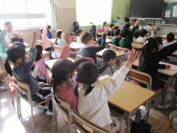 小学校の教室で椅子に座り、発表をしようと挙手をする子供たち