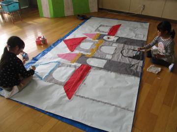 大きな紙にお城をかき、色を塗る子供