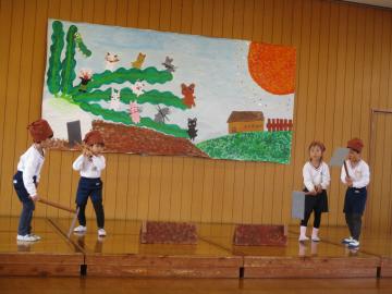 劇でおじいさん役の子供がくわを持って耕す様子