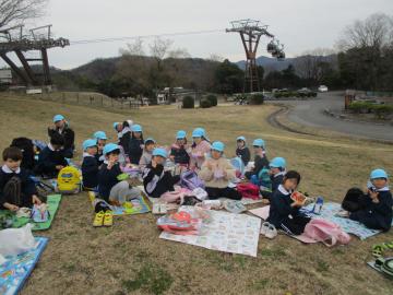 芝生の上でシートを敷いて弁当を食べる子供たち