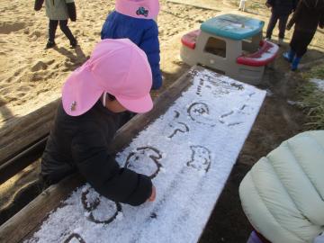 積もった雪に指で絵をかく子供