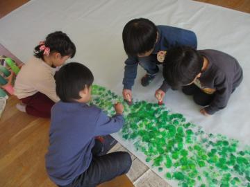 緑の絵の具でスタンピングをしている子供たち