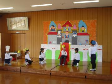 劇で王さま役の子供にひざまずいて挨拶をする家来役の子供たち