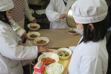 給食当番がひなあられをトレーにのせている様子